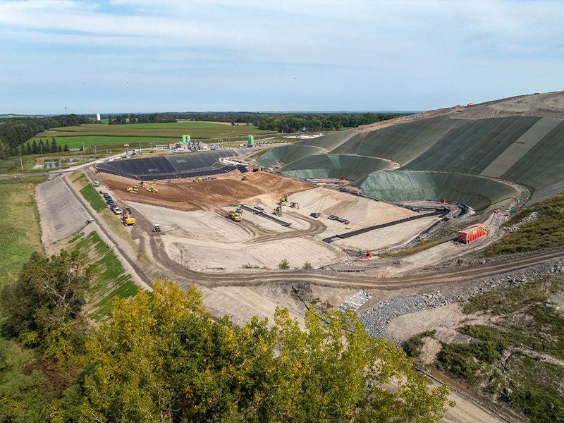 Aerial view of landfill construction with machinery, fields, and trees.
