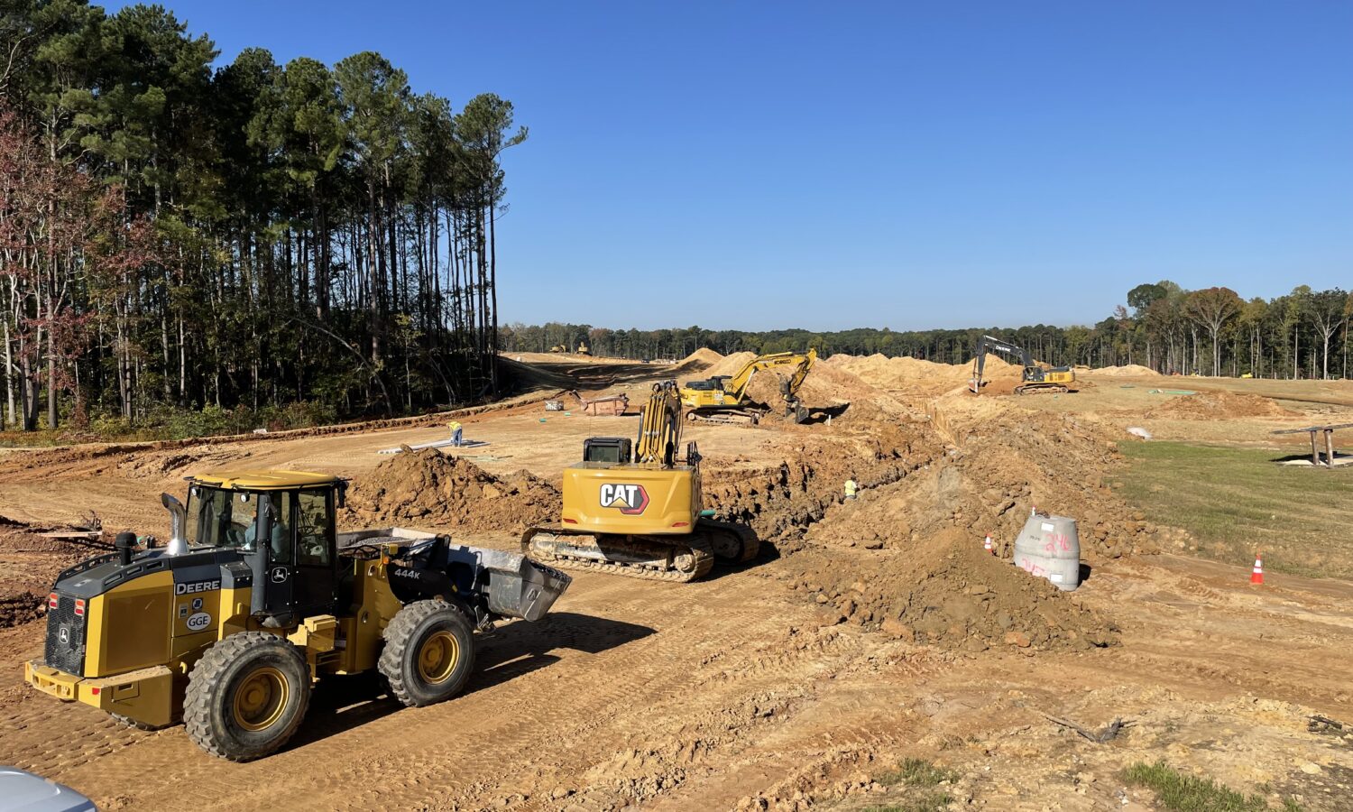 Bulldozers and excavators move dirt on a sunny site.