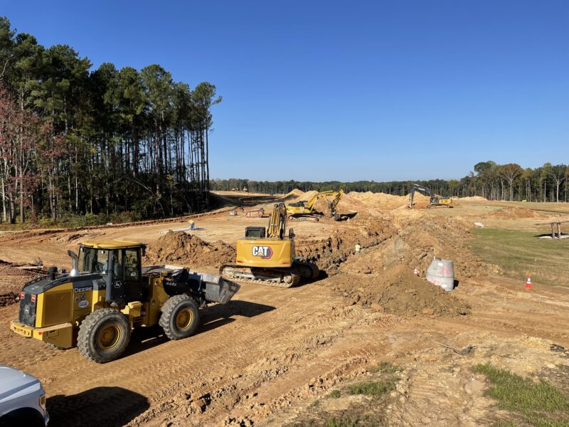 Bulldozers and excavators move dirt on a sunny site.