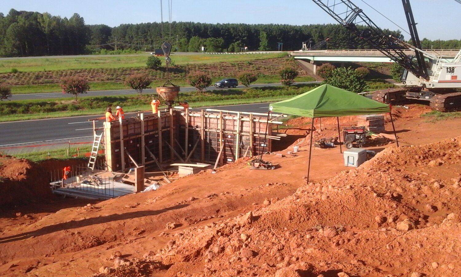 Workers in vests build near highway with crane and canopy.