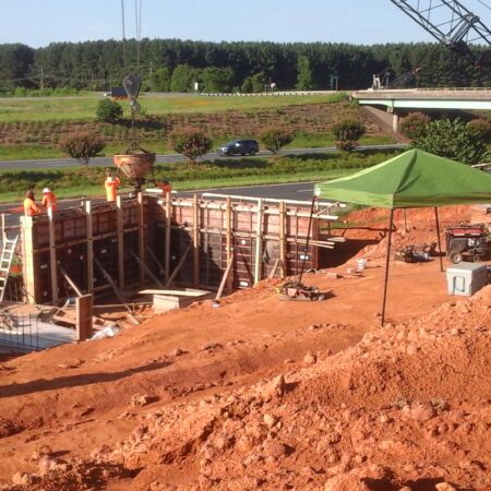 Workers in vests build near highway with crane and canopy.