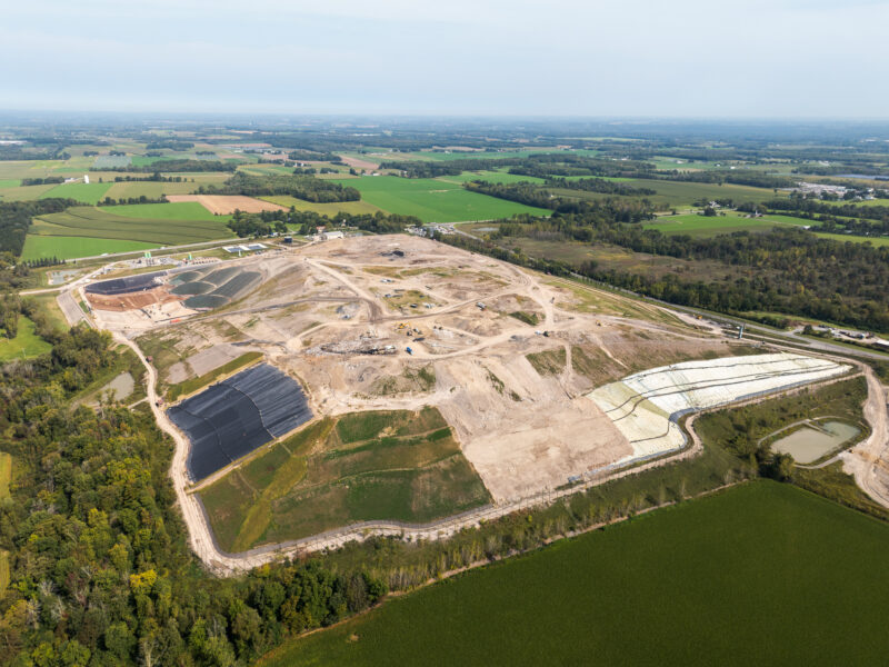 Aerial view: landfill construction amid green fields and forest.