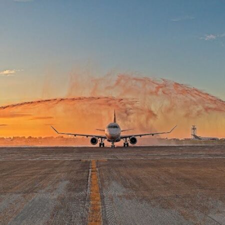Plane on runway greeted by water arches at sunrise.