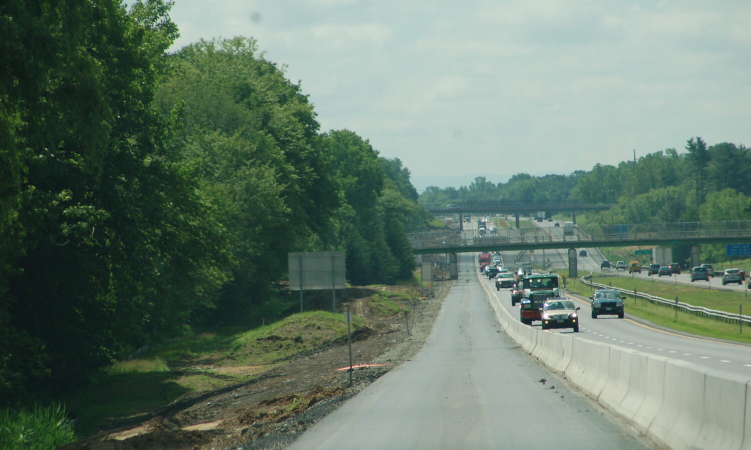 Cars drive in one lane beside barriers; trees, overpasses.