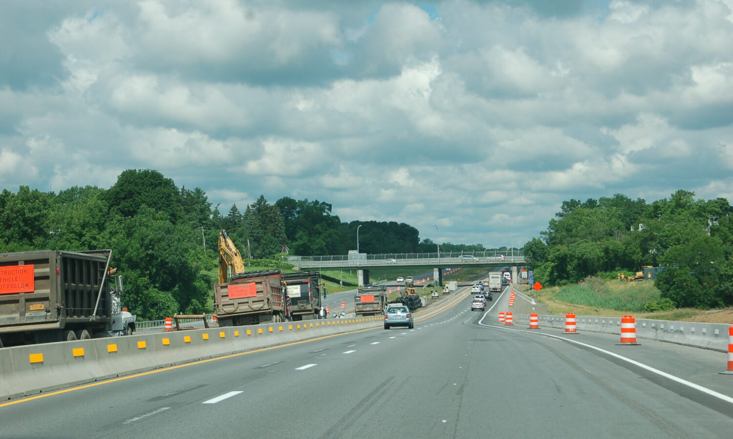 Highway construction left; cars drive both ways under cloudy sky.