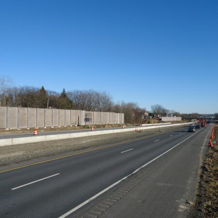 Divided highway under construction, barriers, cones, few cars driving.