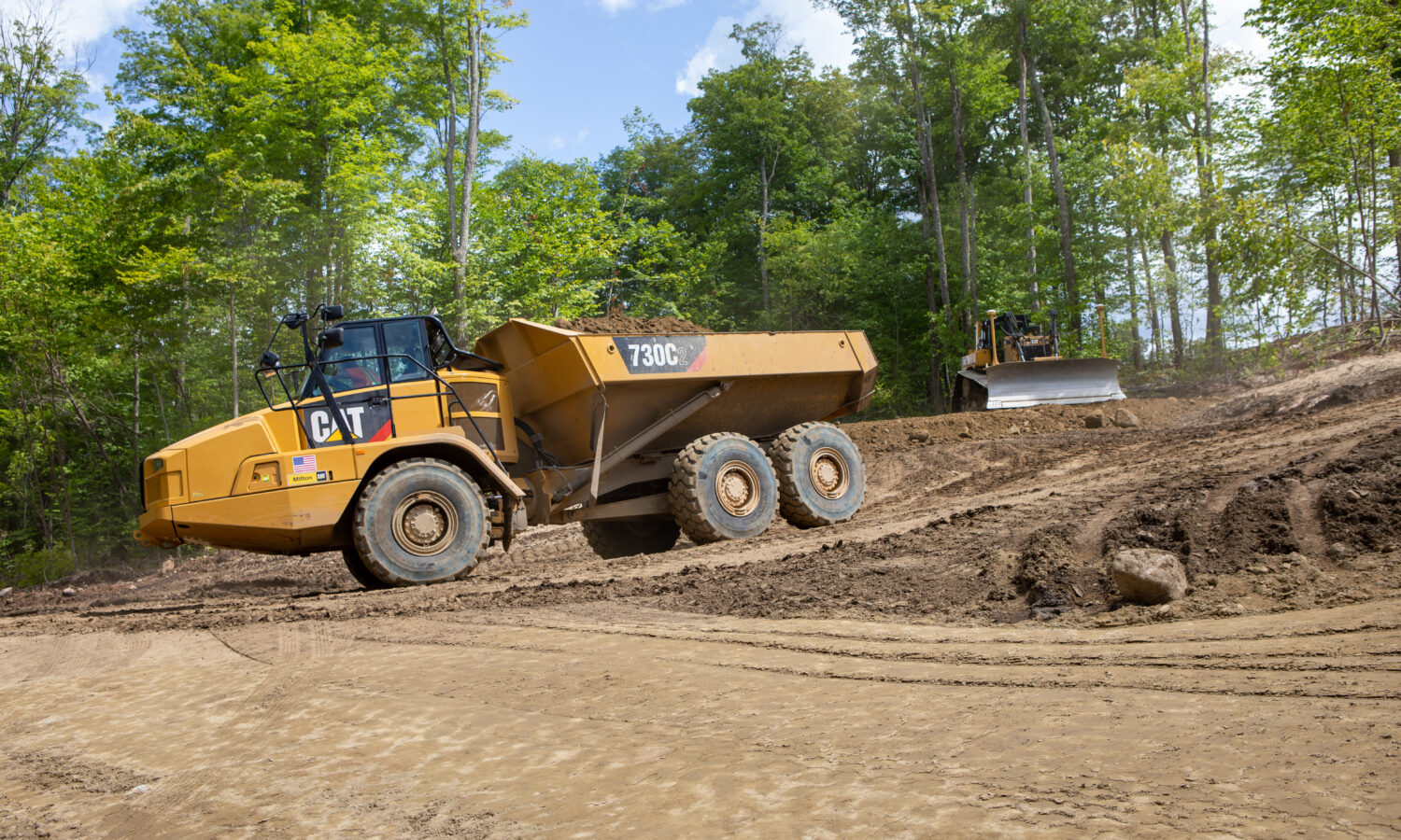 Yellow dump truck and bulldozer work on dirt site.