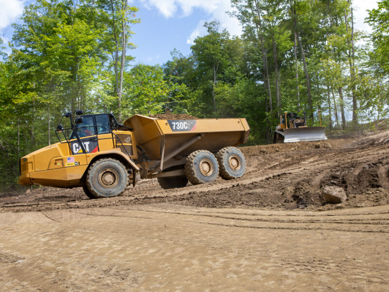 Yellow dump truck and bulldozer work on dirt site.