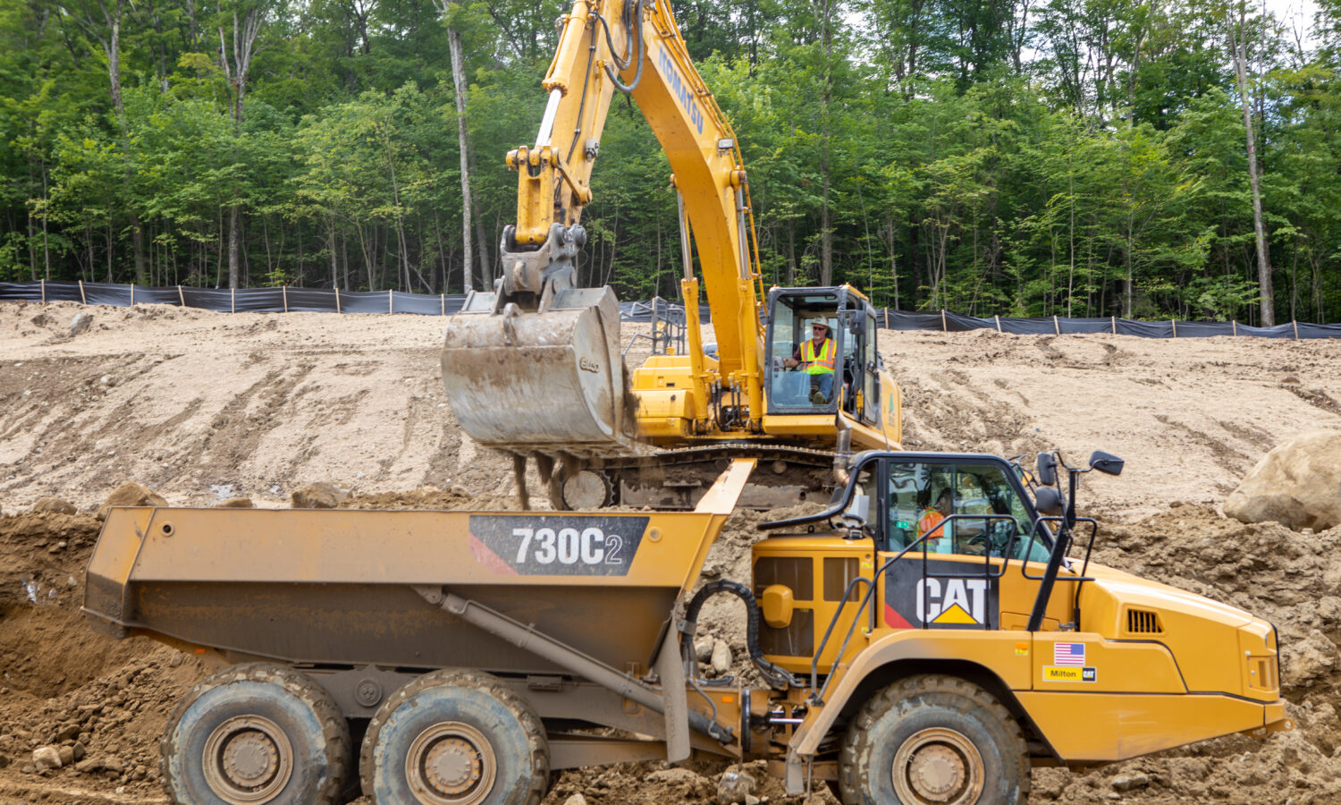 Excavator loads dirt into yellow dump truck at worksite.