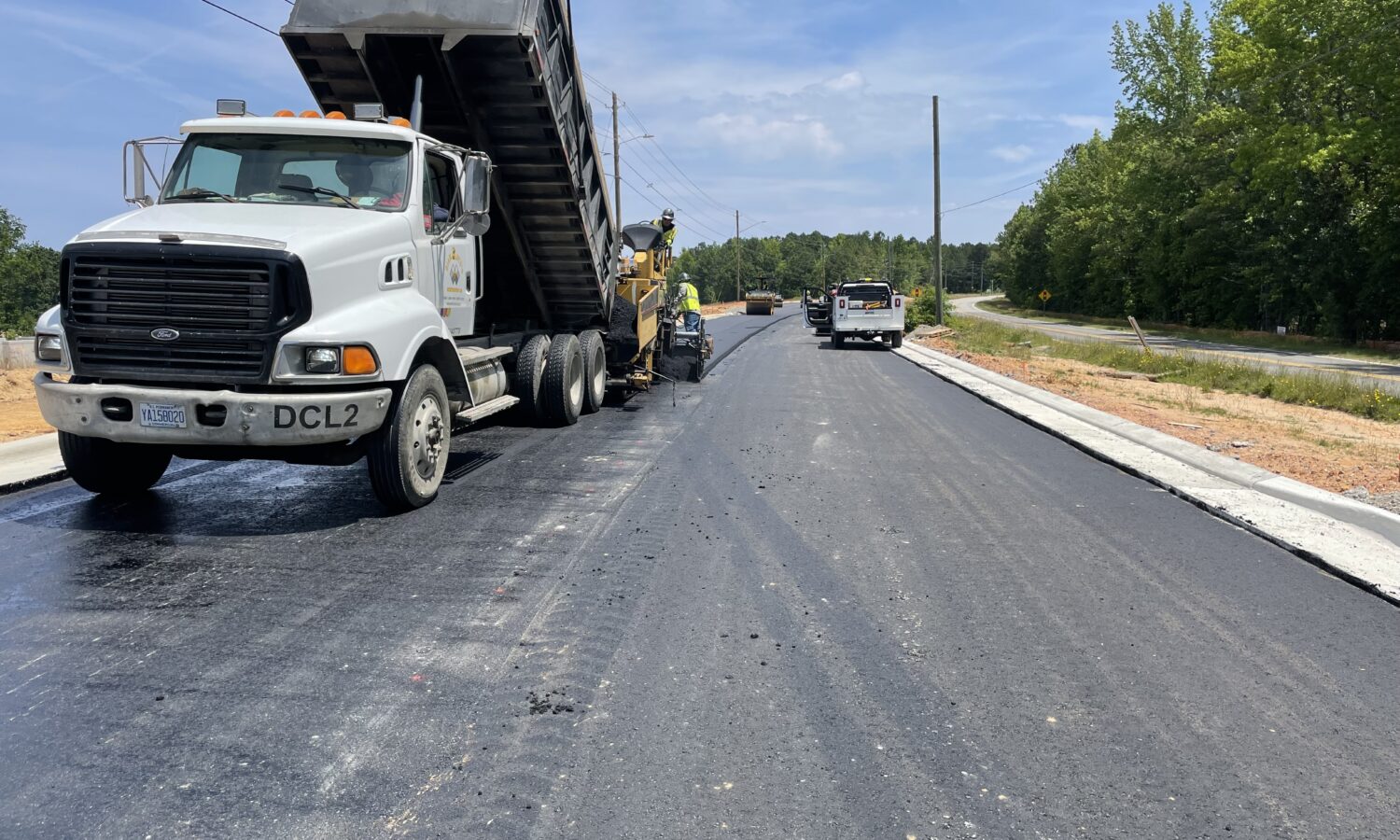 Dump truck unloads asphalt; construction vehicles work under clouds.