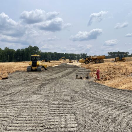 Heavy machinery builds gravel road under partly cloudy sky.