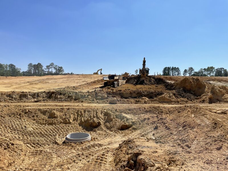 Excavators move earth near dirt piles and drainage pipe.
