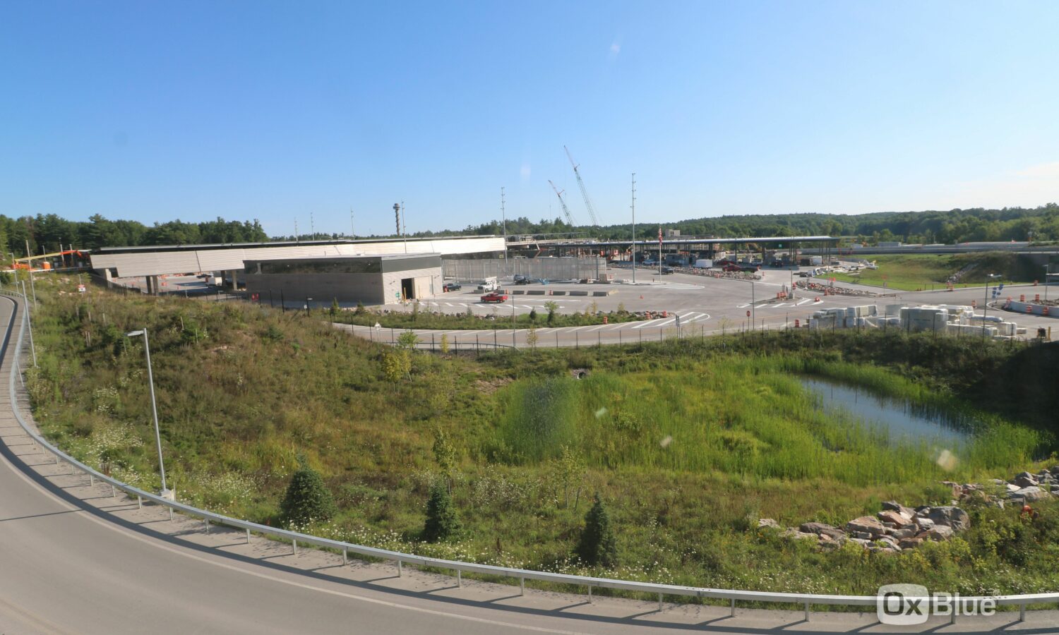 Construction site with cranes, vehicles, greenery, and pond.