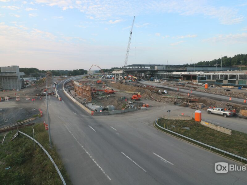 Highway construction with heavy machinery, crane, barriers, and cones.