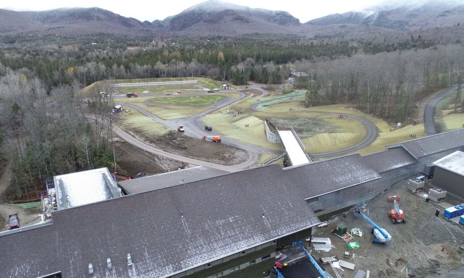 Aerial view: unfinished building, vehicles, landscaping, trees, mountains.
