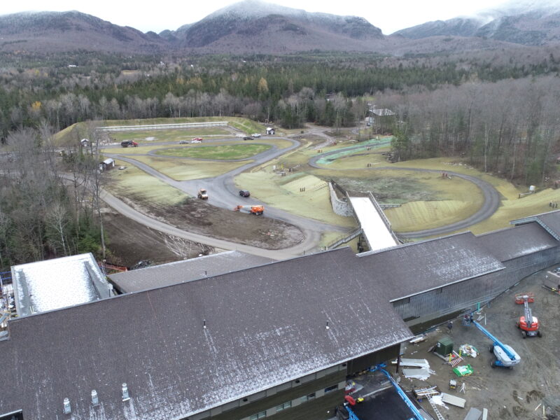 Aerial view: unfinished building, vehicles, landscaping, trees, mountains.