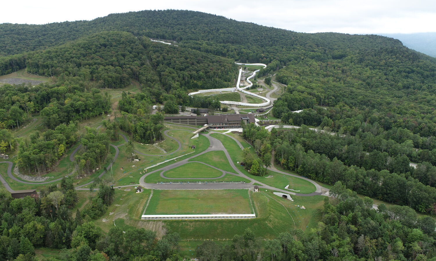 Aerial view: bobsled track winding through dense green forest.