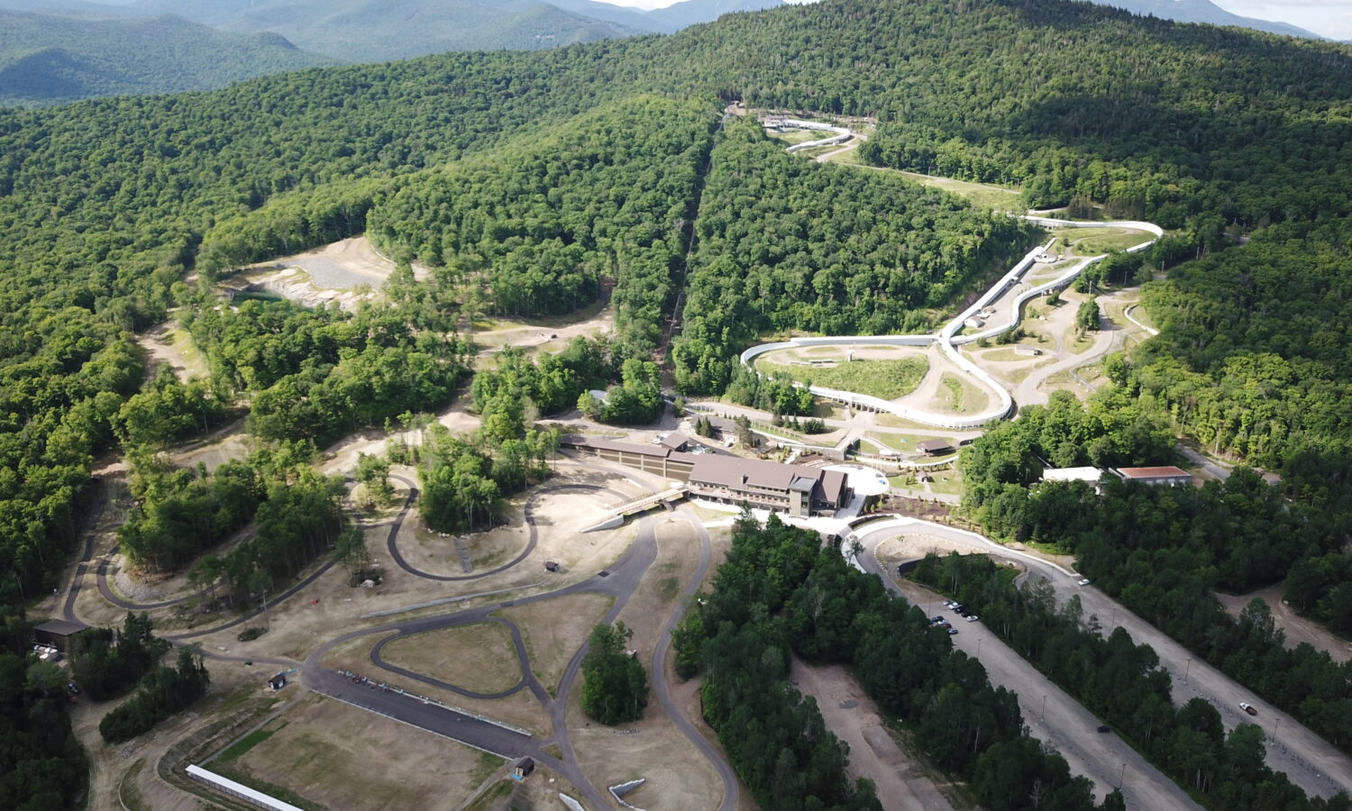 Aerial view of winding bobsled track amid forested mountains.