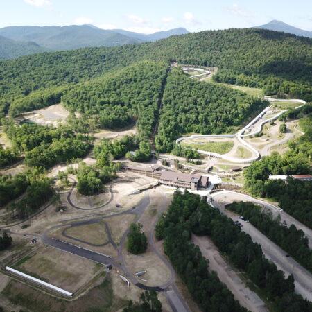 Aerial view of winding bobsled track amid forested mountains.