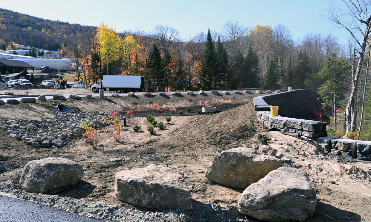 Construction site with rocks, shrubs, and stone wall.