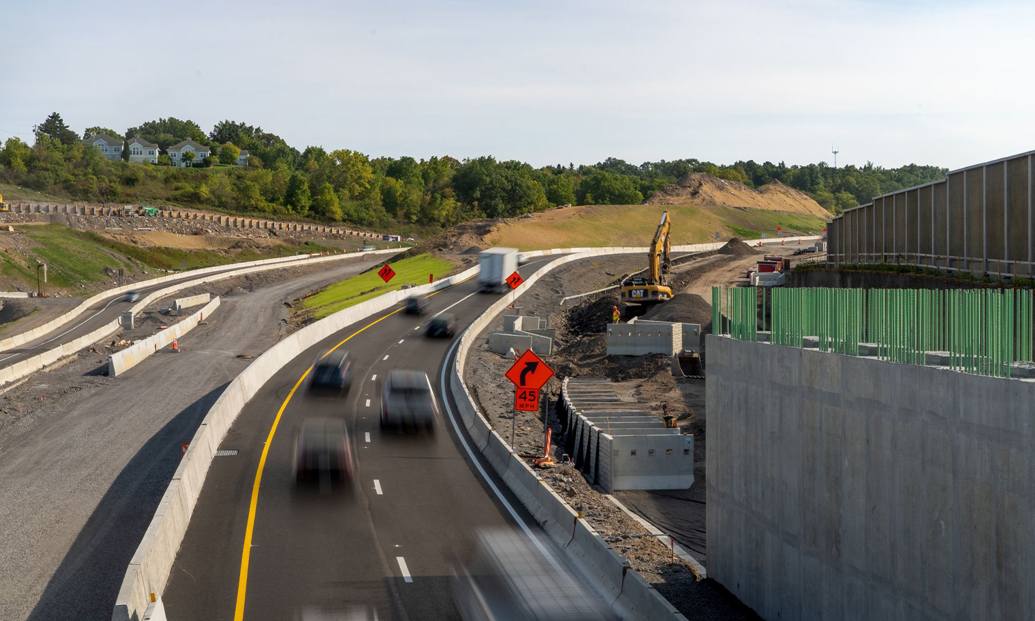 Highway construction zone with traffic, equipment, barriers, and signs.