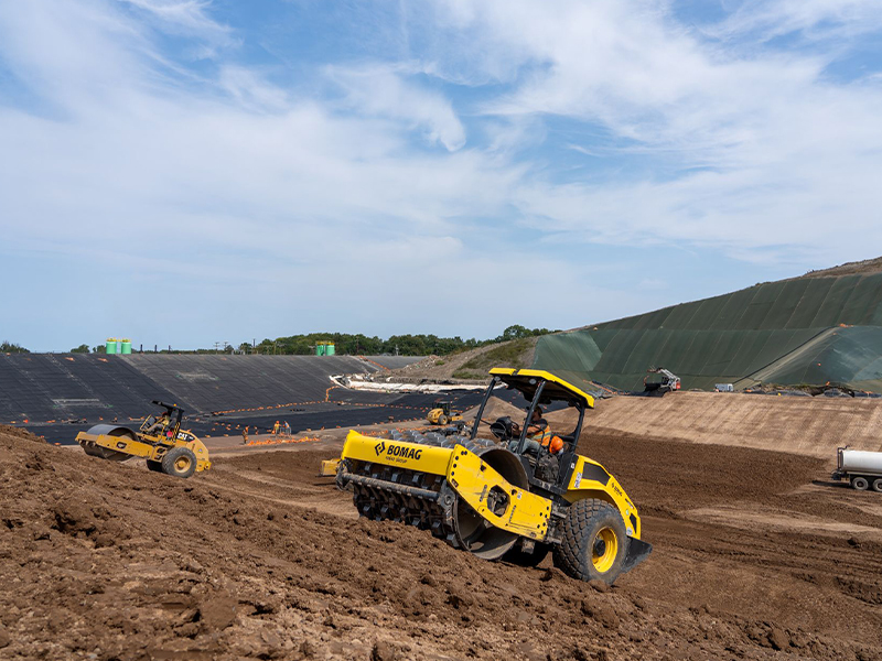 Two yellow compactors work on a sloped dirt construction site.