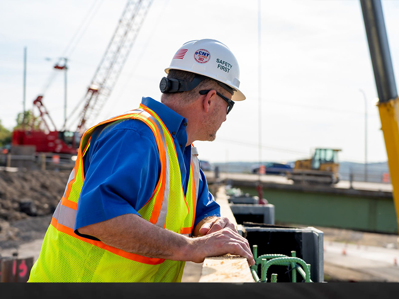 Construction worker in safety gear observes site with cranes.