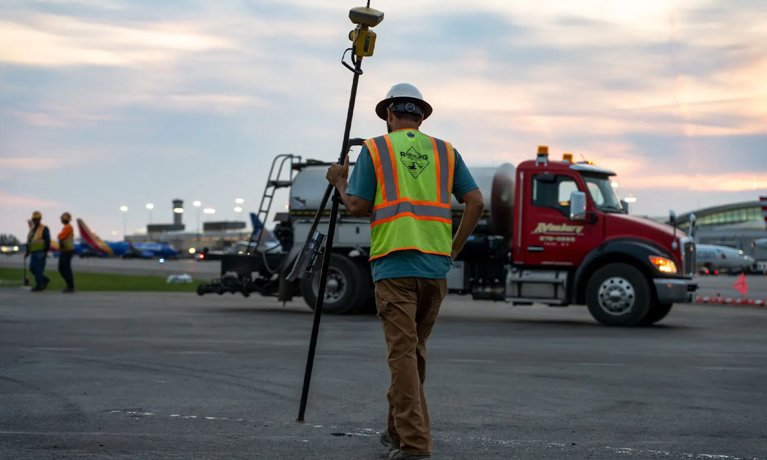 Construction worker with survey gear on the tarmac at dusk.