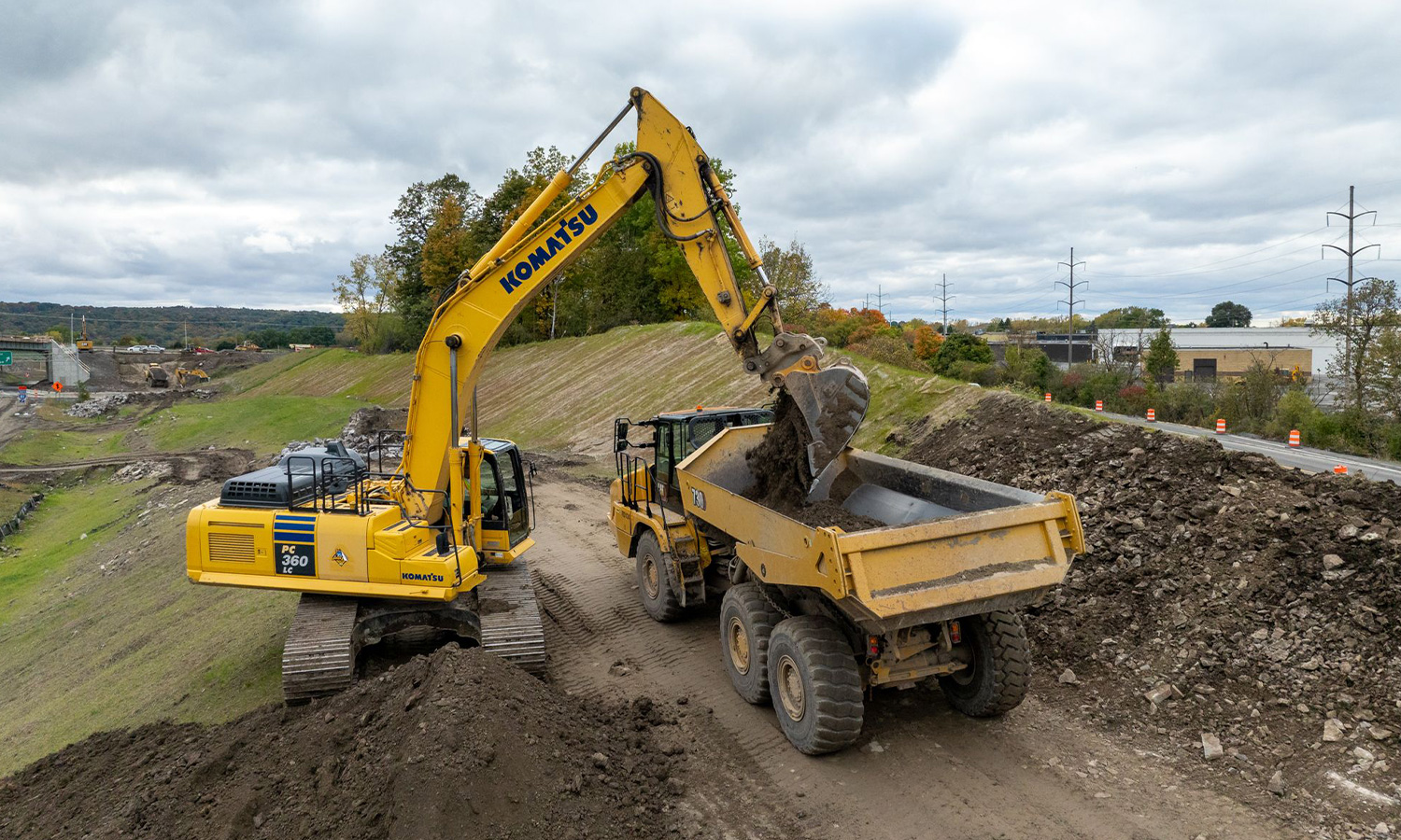 Yellow excavator loads dirt into dump truck on site.